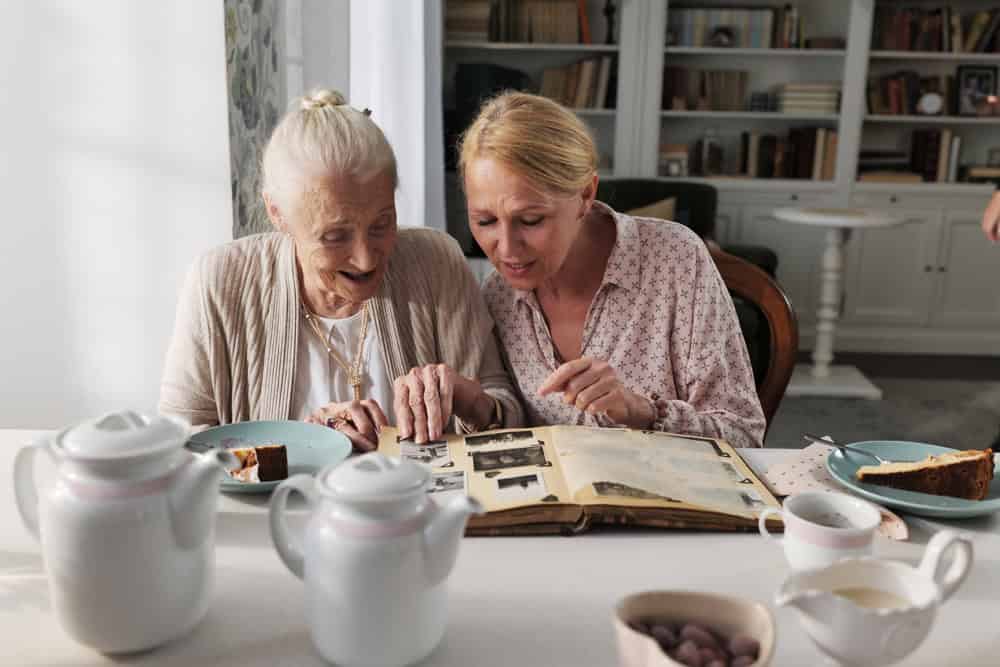 Pflegerin sitzt mit einer älteren Dame am Tisch und schauen ein Fotoalbum an