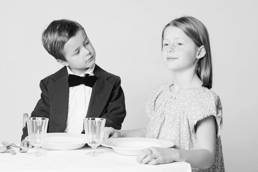 2 Kinder sitzen schick angezogen an einem Tisch