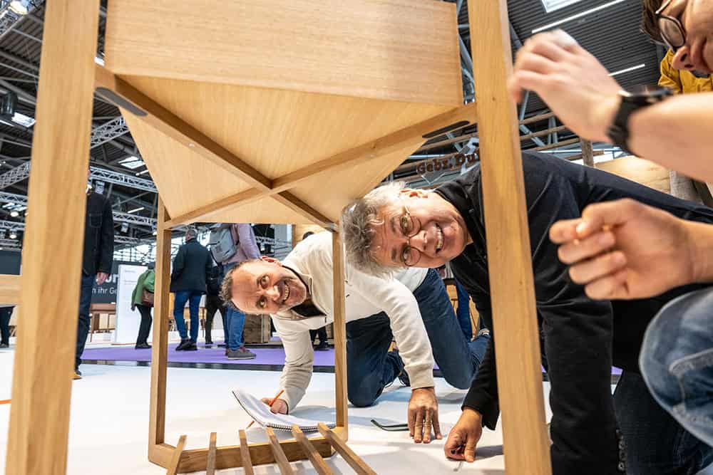 Besucher einer Messe schauen sich ein Möbelstück genau an